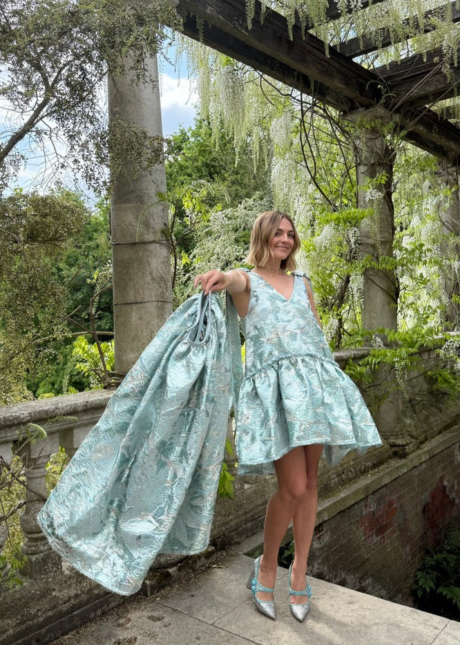 Woman holding a light blue dress in a garden setting